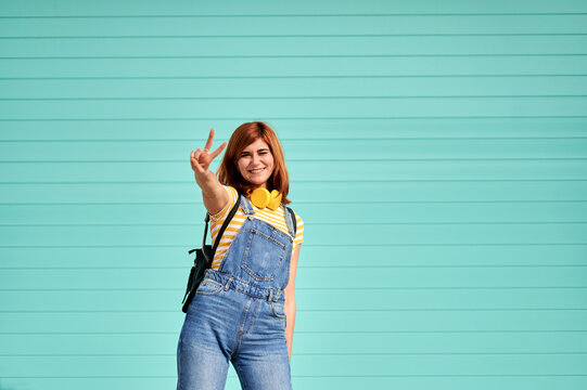 Young woman showing peace sign against turquoise wall against a light blue background