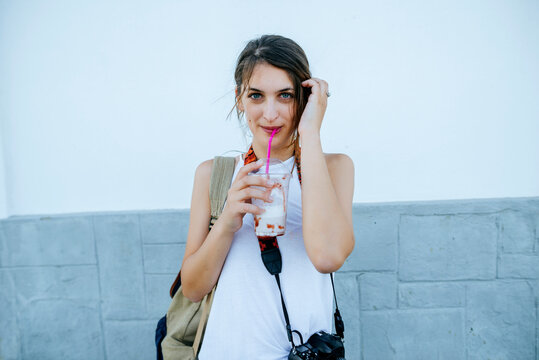 Woman drinking milkshake outdoors, looking at camera