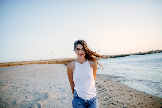 Young woman walking on the beach looking at camera.