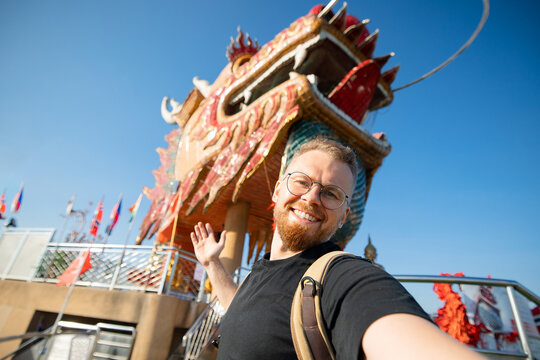 Young male tourist at wat samphran, iconic pink buddhist temple with a dragon in thailand