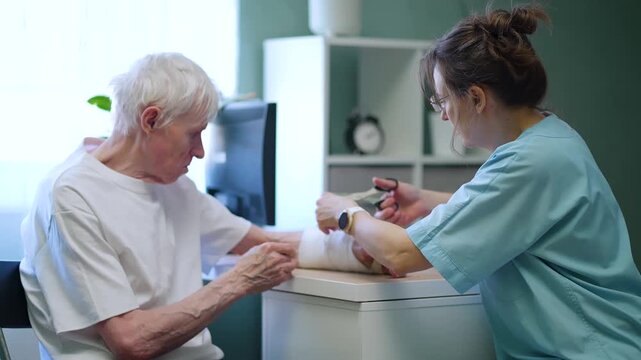 Compassionate nurse carefully changes dressing on senior patient arm in clinic. Professional caregiver provides gentle healing support to vulnerable elderly man recovering from injury.