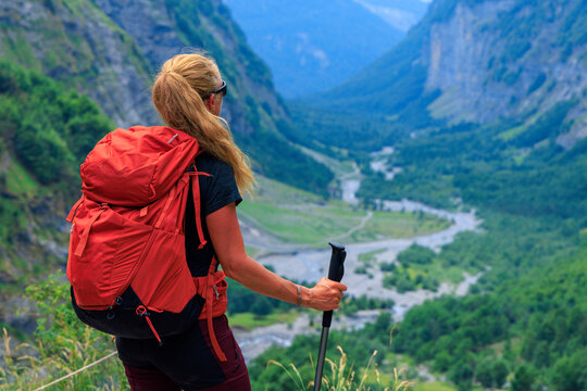 Female hiker with red backpack looking at mountain valley rear view trekking adventure freedom