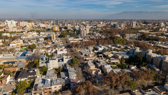 Aerial view of the city of San Juan, featuring a dense urban landscape with residential buildings, tree-lined streets, and distant mountains in San Juan, San Juan Province, Argentina.
