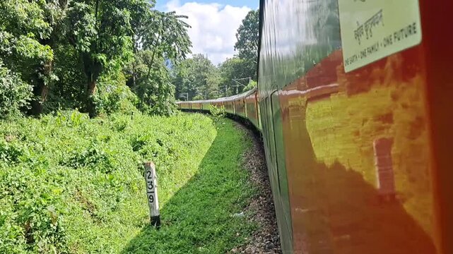Side view of an express train carriage traveling through lush green forests in India