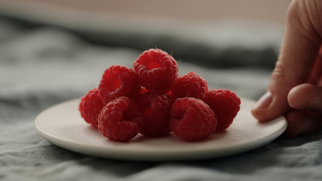 man hand put fresh ripe raspberries on a white saucer