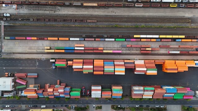 Aerial view of the Osthafen container terminal with stacks of colorful shipping containers, railway tracks with freight trains, and nearby roads in Frankfurt am Main, Hessen, Germany.