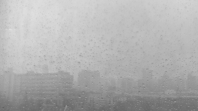 rain droplets covering a glass window with a blurred, overcast cityscape visible in the background