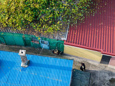 Aerial view of a traditional courtyard in Zemun with vibrant blue, red, and green corrugated metal rooftops, a brick chimney, and a person walking in Belgrade, City of Belgrade, Serbia.