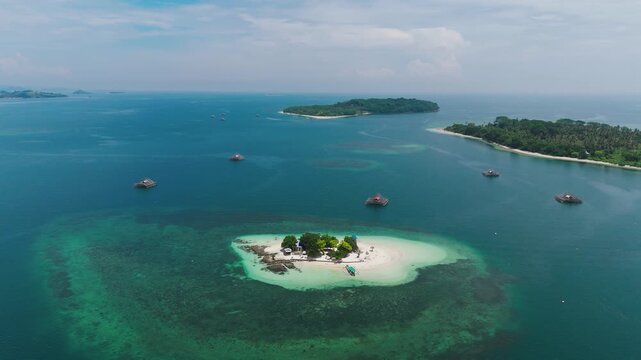 Gili Kedis tiny island aerial view, turquoise lagoon, coral reef patterns, traditional boats anchored, distant green island, Lombok Indonesia coastline, tropical seascape. Aerial drone orbit shot