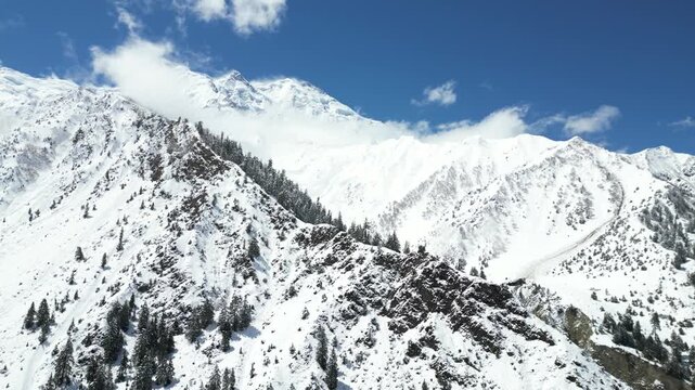 Aerial Drone Flight Along Snow Covered Rakaposhi Mountain and Glacier in Hunza Valley Pakistan with Stunning Karakoram Peaks Under Blue Sky