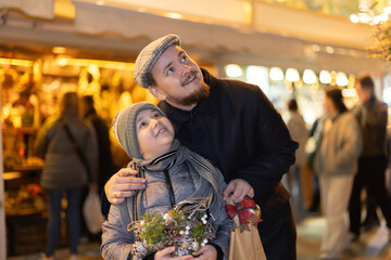 Obraz premium Boy with father stands at fair decorated for New Year holidays, examine surrounding festive exciting atmosphere. They look into distance, try to see something entertaining in distance at festive event
