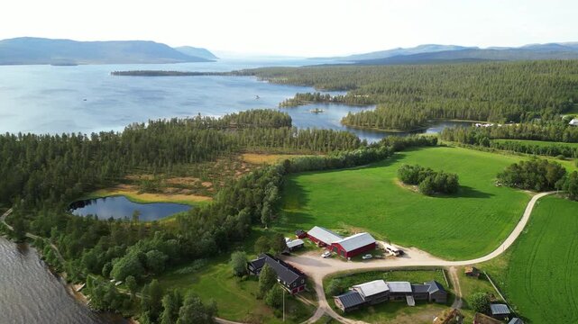 Aerial view of the Femund farm surrounded by lush green fields, dense forest, and the expansive lake in Sorken, Innlandet, Norway.