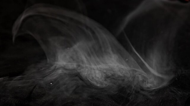 A white smoke cloud in the shape of a wave that disperses against a black backdrop