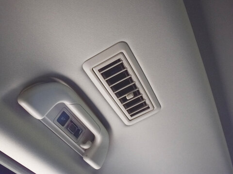 Close-up view of a modern car interior ceiling featuring an air conditioning ventilation grille vent alongside an overhead passenger grab handle with built-in reading light and coat hook