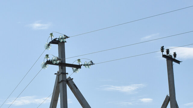 Electricity transmission line concrete utility poles with electrical wires, glass and ceramic insulators under a clear blue sky on a bright day with copy space