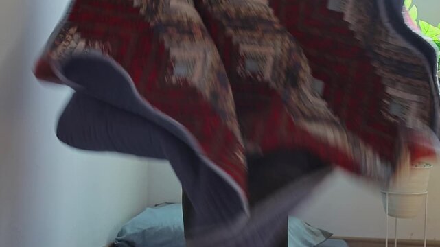 Man holding up and neatly folding heavy quilted blanket in bright room