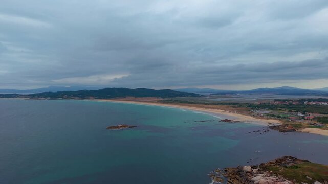 Aerial - the long sweep of A Lanzada beach with rocky islets dunes and hills in Pontevedra Galicia