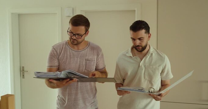 Two colleagues review documents and binders together, discussing paperwork and checking information. Concept of teamwork, administration, document management, and collaboration.