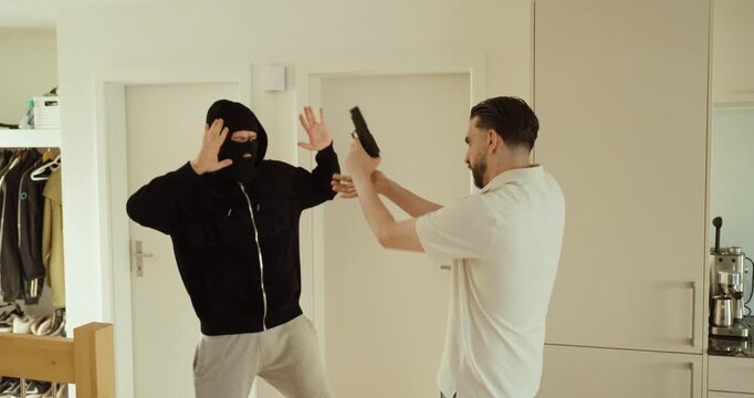 A homeowner defends himself during a home invasion, disarming an armed robber and taking control of the handgun. Concept of self-defense, personal safety, and crime prevention.