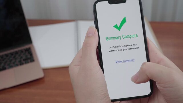 Hands hold a smartphone showing an AI notice that a document summary is complete in a modern workspace.