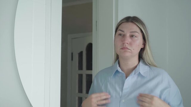Job seeker in a loose button-up smooths her shirt and steadies herself during a final wardrobe check for a remote job meeting.