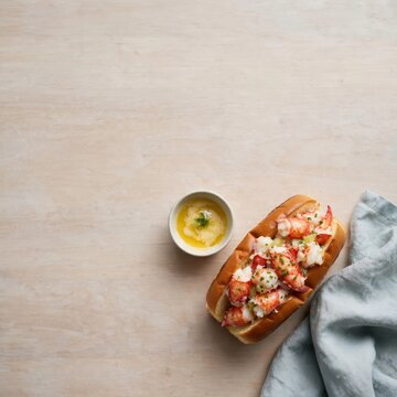Fresh lobster roll with melted butter on a wooden table, National Lobster Day celebration, seafood restaurant menu or dining concept