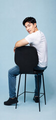 Fototapeta premium Confident Young Asian Man Sitting on Chair in Minimalist Studio, Modern Business Lifestyle Portrait