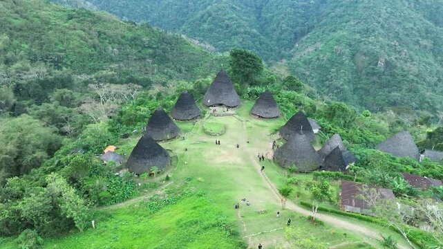 Aerial view of Waerebo Village with traditional conical houses surrounded by lush green mountains in Satar Mese Barat, East Nusa Tenggara, Indonesia.