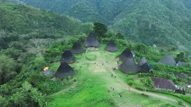 Aerial view of the traditional conical houses of Waerebo Village surrounded by lush green mountains in Satar Mese Barat, East Nusa Tenggara, Indonesia.