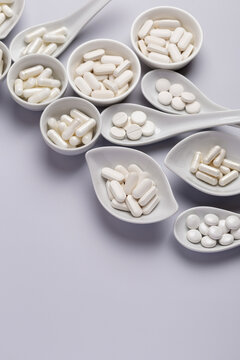 White pills and tablets in white ceramic spoons and white ceramiv bowls on white background from above. Dietary supplements, vitamins and minerals to improve immune system and health. 