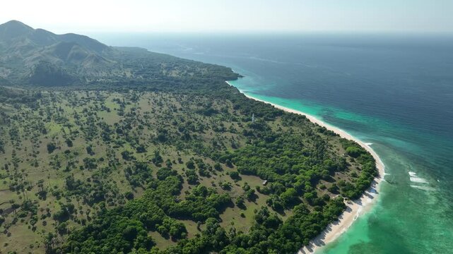 Aerial view of Nuca Molas island featuring lush green vegetation, a white sandy beach, and turquoise coastal waters in Satar Mese Barat, East Nusa Tenggara, Indonesia.