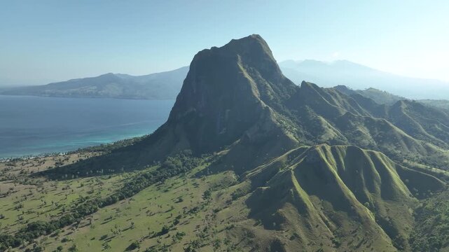 Aerial view of Nuca Molas island featuring a prominent rocky peak, lush green slopes, and the surrounding blue sea in Satar Mese Barat, East Nusa Tenggara, Indonesia.