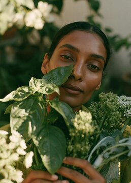 Close-up portrait of a young woman holding a bunch of flowers. she is looking directly at the camera with a serious expression on her face. the woman has dark hair and is wearing a green top.