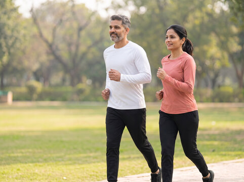 Indian couple synchronized jogging in a premium green park representing fitness wellness preventive health companionship and active lifestyle