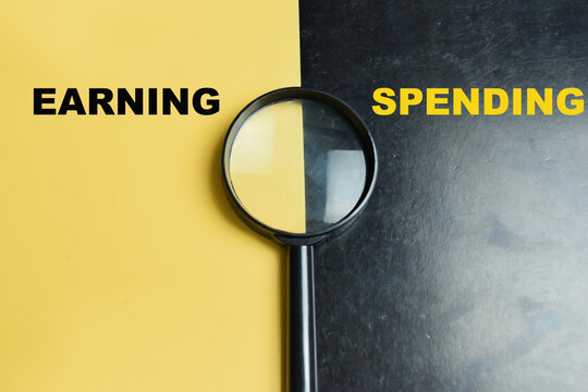 Concept of earning or spending write on color background with magnifying glass.
