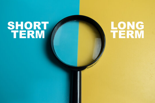 Concept of short term or long term write on color background with magnifying glass.
