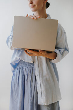 Woman In Light Blue Oversized Linen Shirt Holding Closed Laptop Computer In Front Of Chest