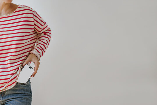 Woman In Red And White Striped Long Sleeve Top Putting Smartphone Blank Screen Mockup Into Denim Jeans Pocket