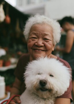Close-up portrait of an elderly woman with white hair, smiling widely and looking at the camera. she is holding a small white dog in her arms.