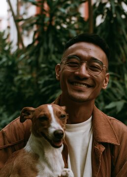 Portrait of a young man with a big smile on his face. he is wearing a brown leather jacket and a white t-shirt. he has short black hair and is wearing glasses.