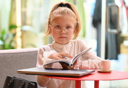 Close-up portrait of a little girl sitting at a table with an open notebook