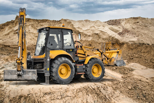 A universal excavator loader is at a construction site. The machine is moving dirt and shaping the ground for future building projects under a cloudy sky