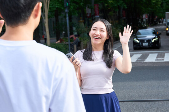 Young Japanese Man and Woman Waving and Greeting Each Other on City Street
