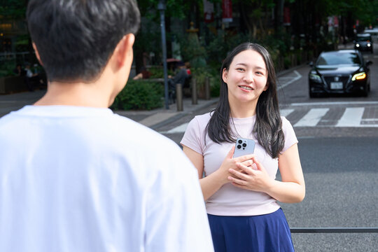 Young Japanese Man and Woman Waving and Greeting Each Other on City Street