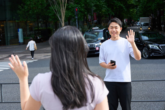 Young Japanese Man and Woman Waving and Greeting Each Other on City Street