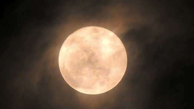 Full moon glows brightly behind thin dark clouds in the night sky.