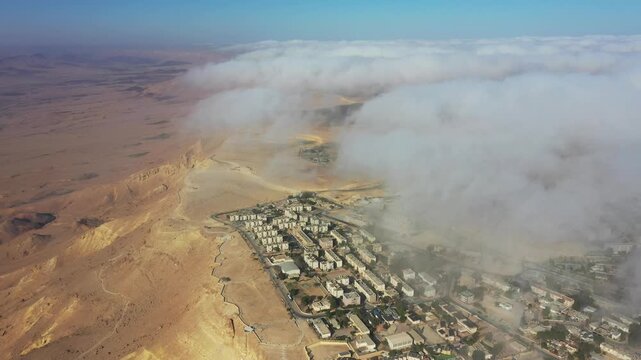 Aerial view of Mitzpe Ramon town nestled on the edge of the Ramon Crater with low clouds rolling over the desert landscape in Mitzpe Ramon, South District, Israel.