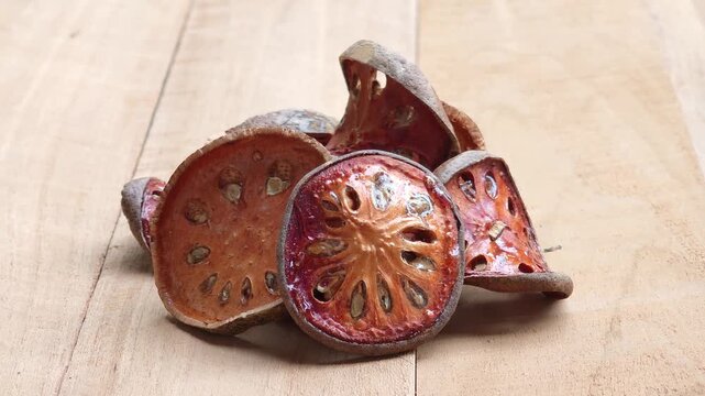Dried bael fruit slices placed on a wooden surface.