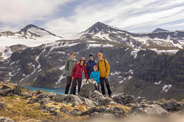 Fototapeta premium Beautiful european family with children and pet dog, hiking Kyrkja mountain on a beautiful sunny summer day, sunset, snow, lakes, valley