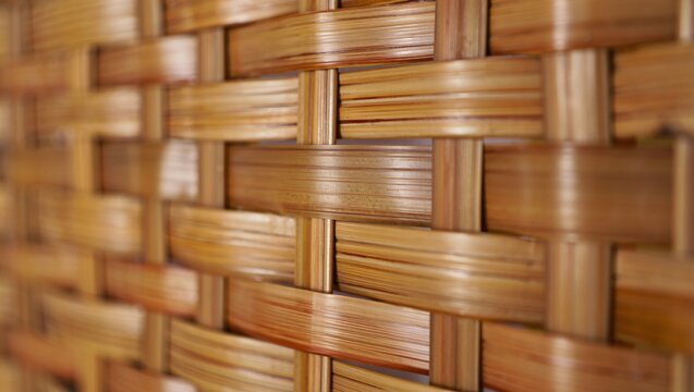 Closeup of a woven bamboo texture background, featuring an intricate pattern of interlaced natural wooden strips with warm brown tones and visible grain details